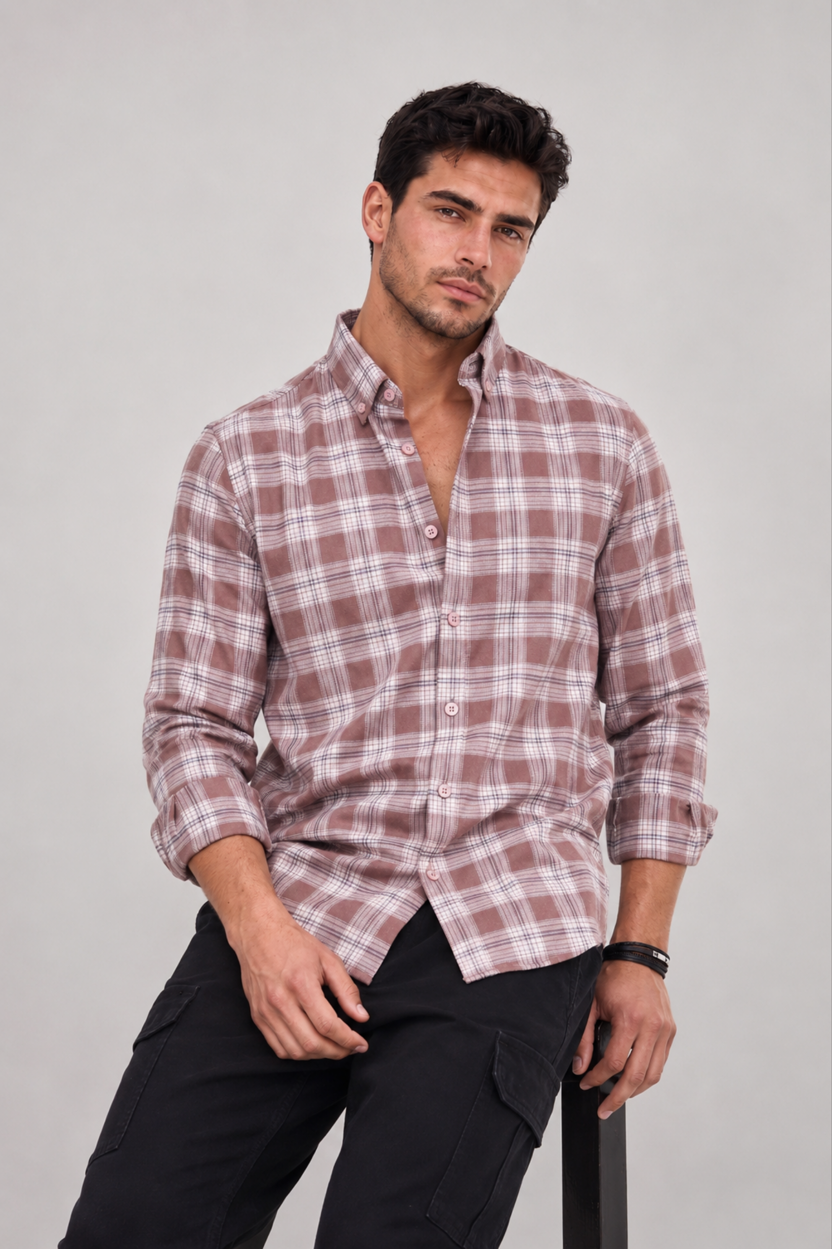 Model seated in GKSEN dusty mauve plaid check shirt for men styled in a smart casual look.