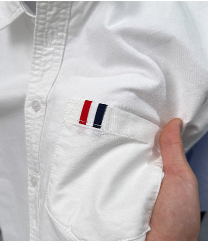 Detailed view of GKSEN men's ivory white Oxford cotton shirt chest pocket, fabric texture and red white navy accent tab
