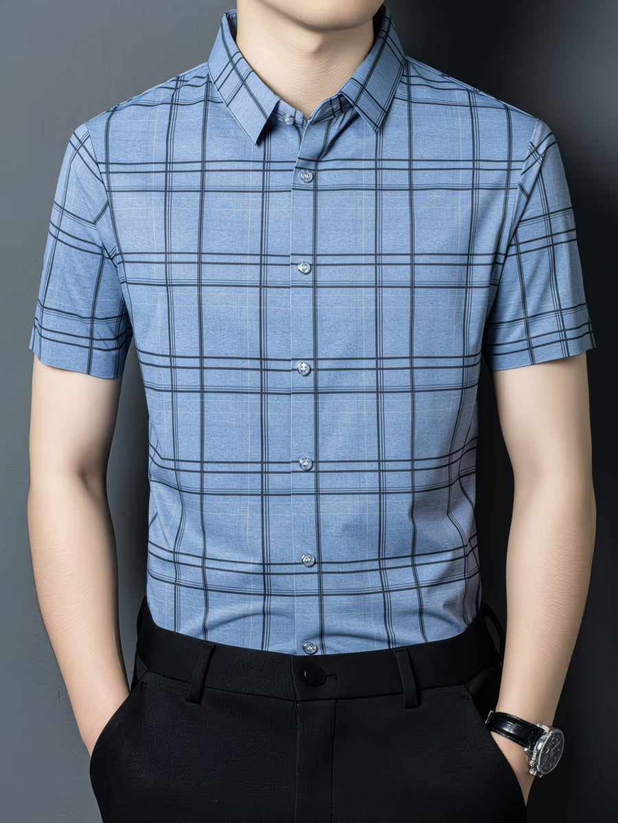 GKSEN denim blue check men’s shirt shown in a front model pose with short sleeves, light buttons, black trousers, and windowpane check pattern.