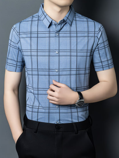 GKSEN denim blue grid check men’s shirt shown in a front model pose with the model adjusting the shirt and short sleeve styling visible.