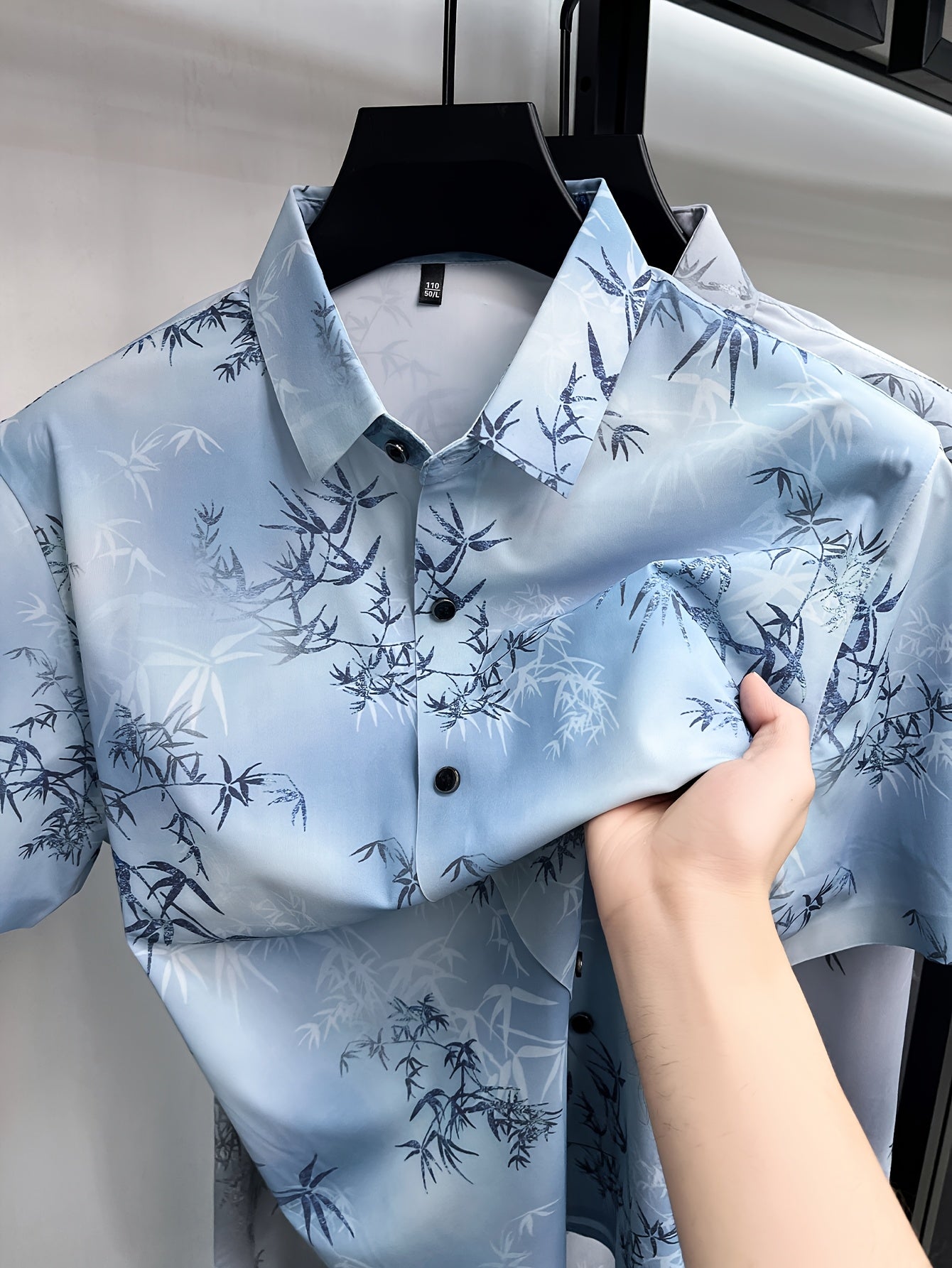 GKSEN men’s shirt in ice blue bamboo print shown on a hanger with the front collar, black buttons, and folded shirt detail visible.