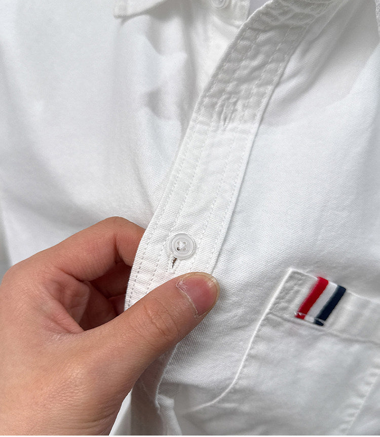 Close-up of GKSEN men's white Oxford cotton shirt showing front button stitching and red white navy chest pocket accent